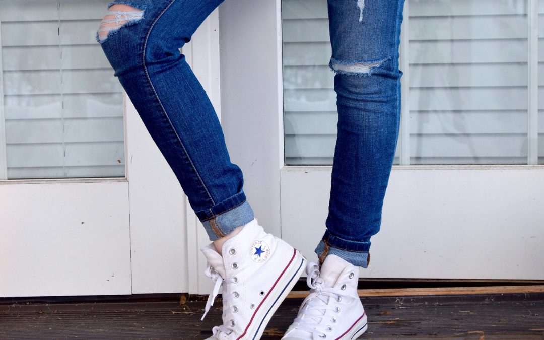 Women’s distressed blue denim jeans and pair of white Converse Allstar high-tops